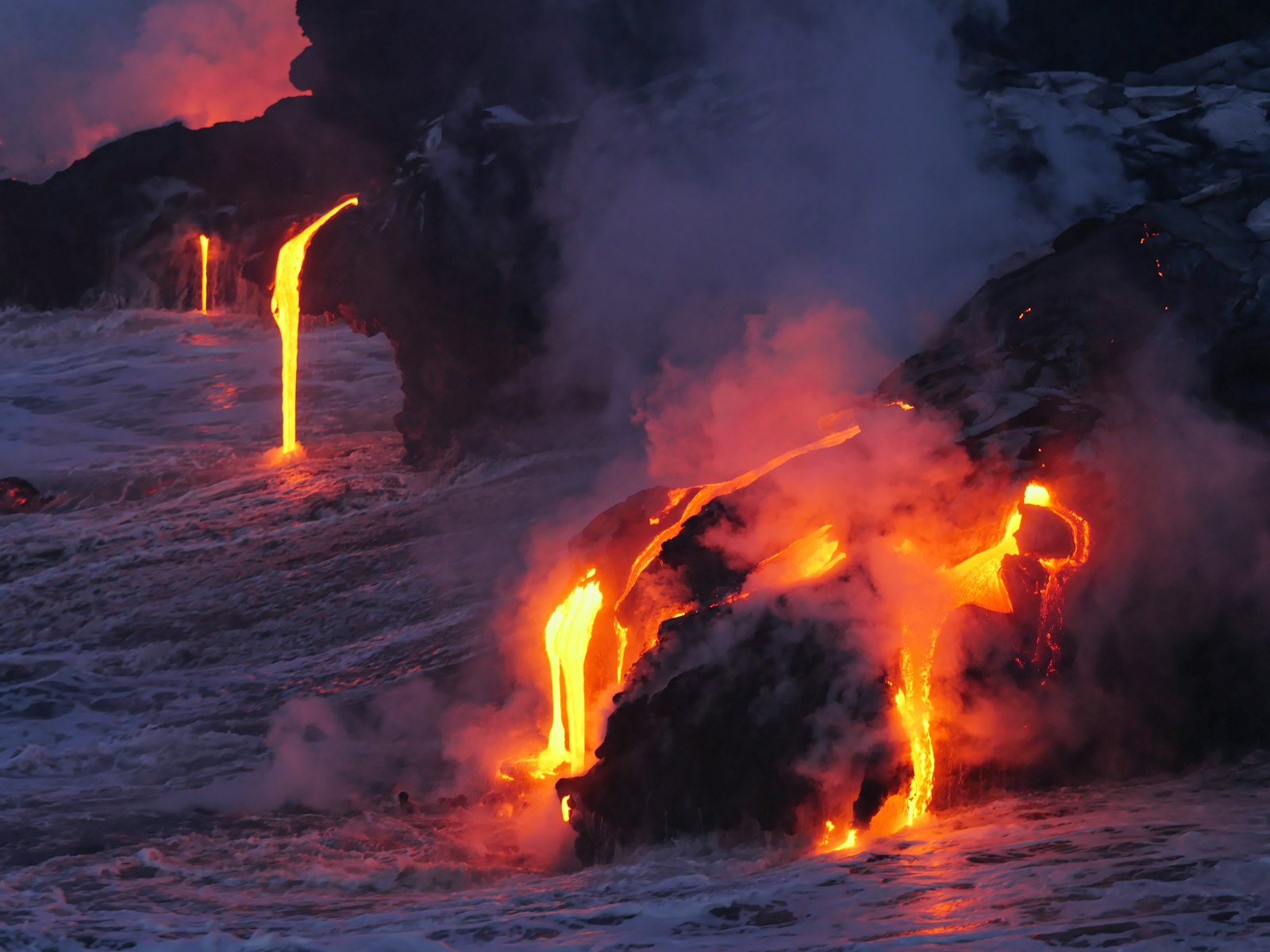 Molten orange lava from Kīlauea volcano flowing across hardened black basalt rock on Hawaii's Big Island
